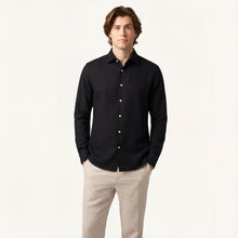 Man wearing a black button-up shirt and beige pants on a white background